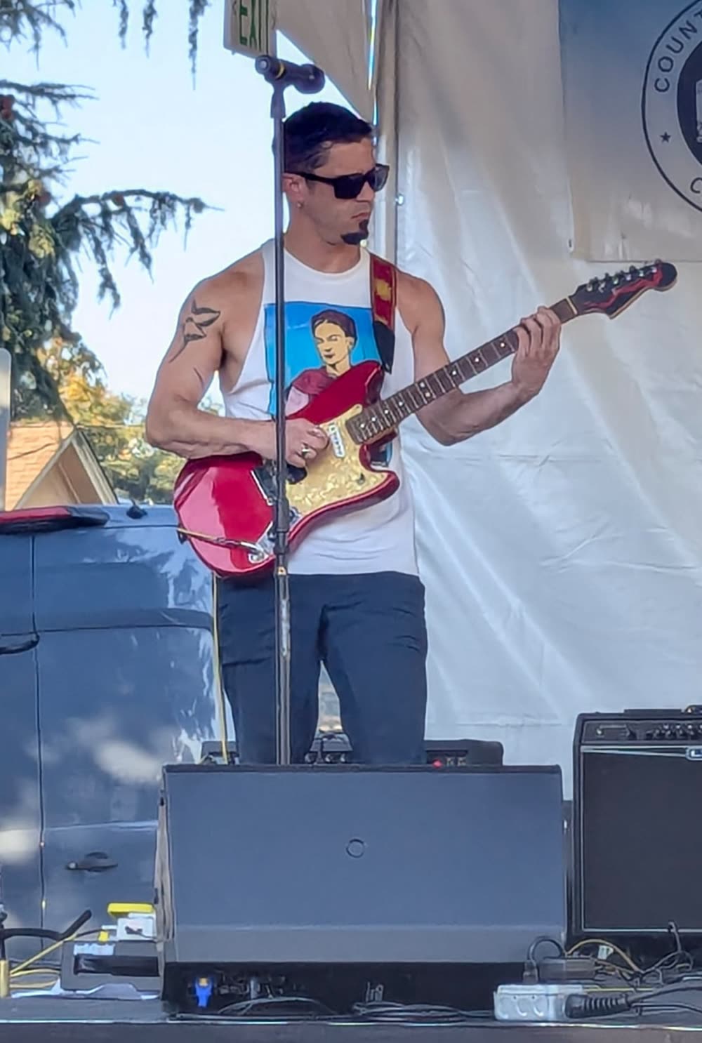 Guitarist in sunglasses playing a red offset guitar.
